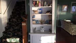 Eine Treppe mit gemustertem Teppich, eine weiße Schrankwand mit Regalen, gefüllt mit Büchern und Dekoration, sowie ein gemustertes Sofa in einem Zimmer mit grünen Wänden.