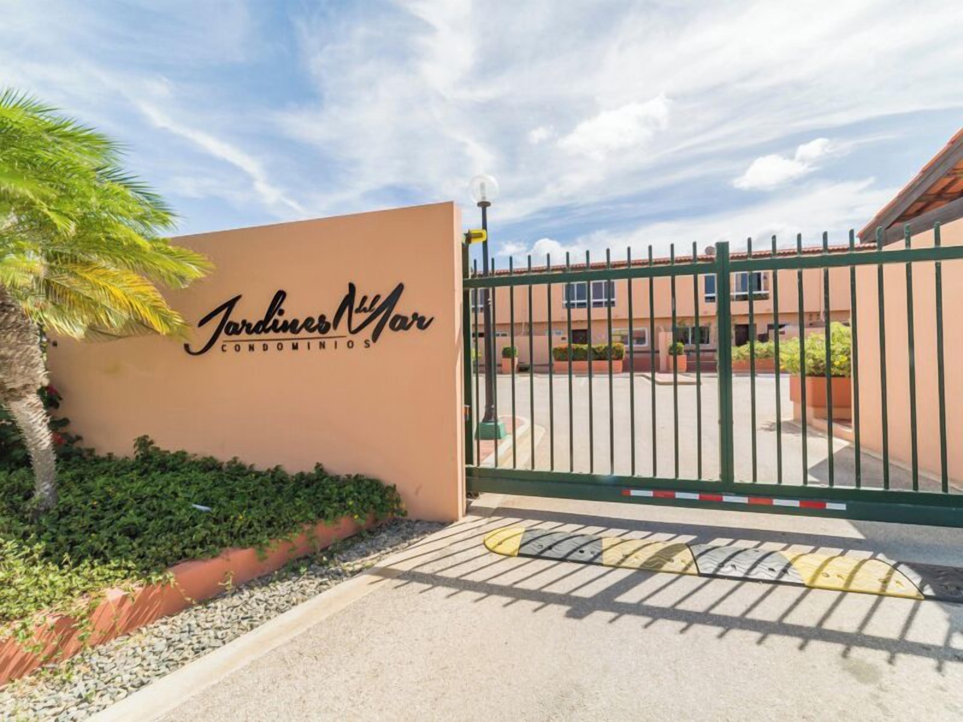 A gated entrance to a residential complex named 'Jardines Nivar condominiums' with a clear sky and a palm tree in the foreground.