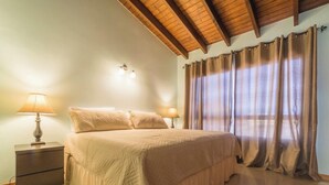 A bedroom with a large bed, two bedside lamps, a nightstand, and a ceiling with wooden beams. - Fabulous, spacious townhome steps from Eagle Beach (Oranjestad)