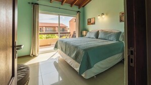 A bedroom with a large bed, a balcony with chairs, and a view of buildings. - Fabulous, spacious townhome steps from Eagle Beach (Oranjestad)