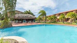 A swimming pool with lounge chairs and a thatched-roof structure. - Fabulous, spacious townhome steps from Eagle Beach (Oranjestad)