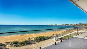 A beach view with a staircase leading down to the shore, clear skies, and a distant shoreline with buildings.