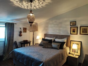 Een slaapkamer met een bed, nachtlampjes, een viool en ingelijste foto’s aan de muur.