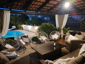 Een terras buiten met een zwembad, rieten meubels en een pergola.