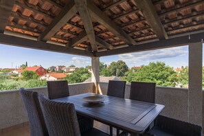 Een overdekt terras met een tafel en stoelen, met uitzicht op een woonwijk.