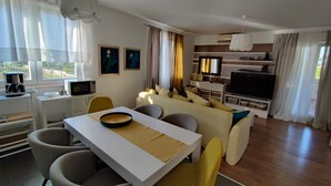 A modern living room with a sofa, dining table, and chairs. There is a TV, a coffee maker, and a microwave. The room has large windows with curtains. - Villa Danica with private pool and WIFI Near Center Of The Town And 2km Beach (Pula)