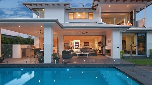 Ein modernes, zweigeschossiges Haus mit Swimmingpool, Sitzbereich im Freien und einem Balkon.