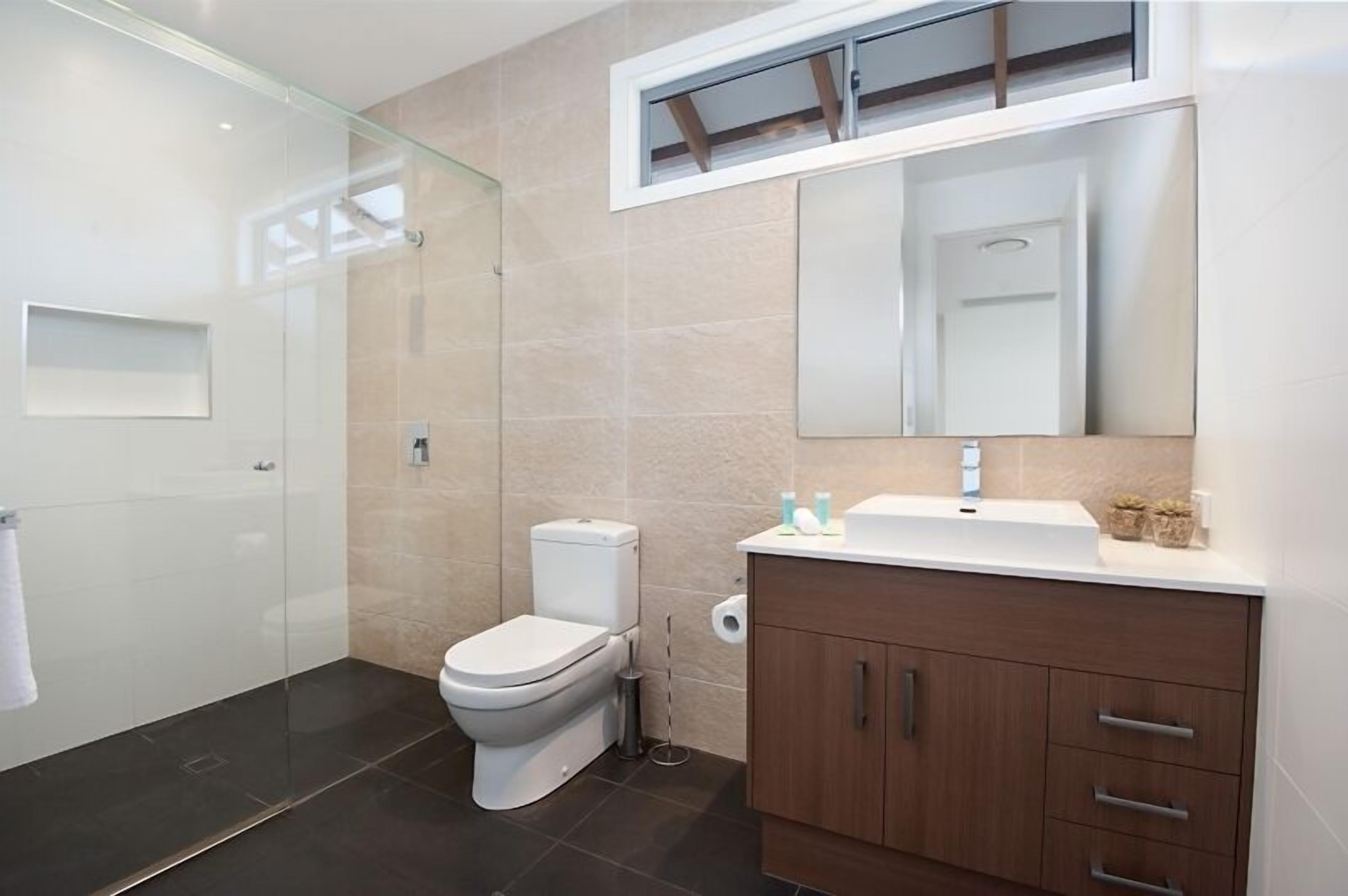 Ein modernes Badezimmer mit Glasdusche, Toilette, Waschbecken mit Spiegel und einem Schrank mit Schubladen.