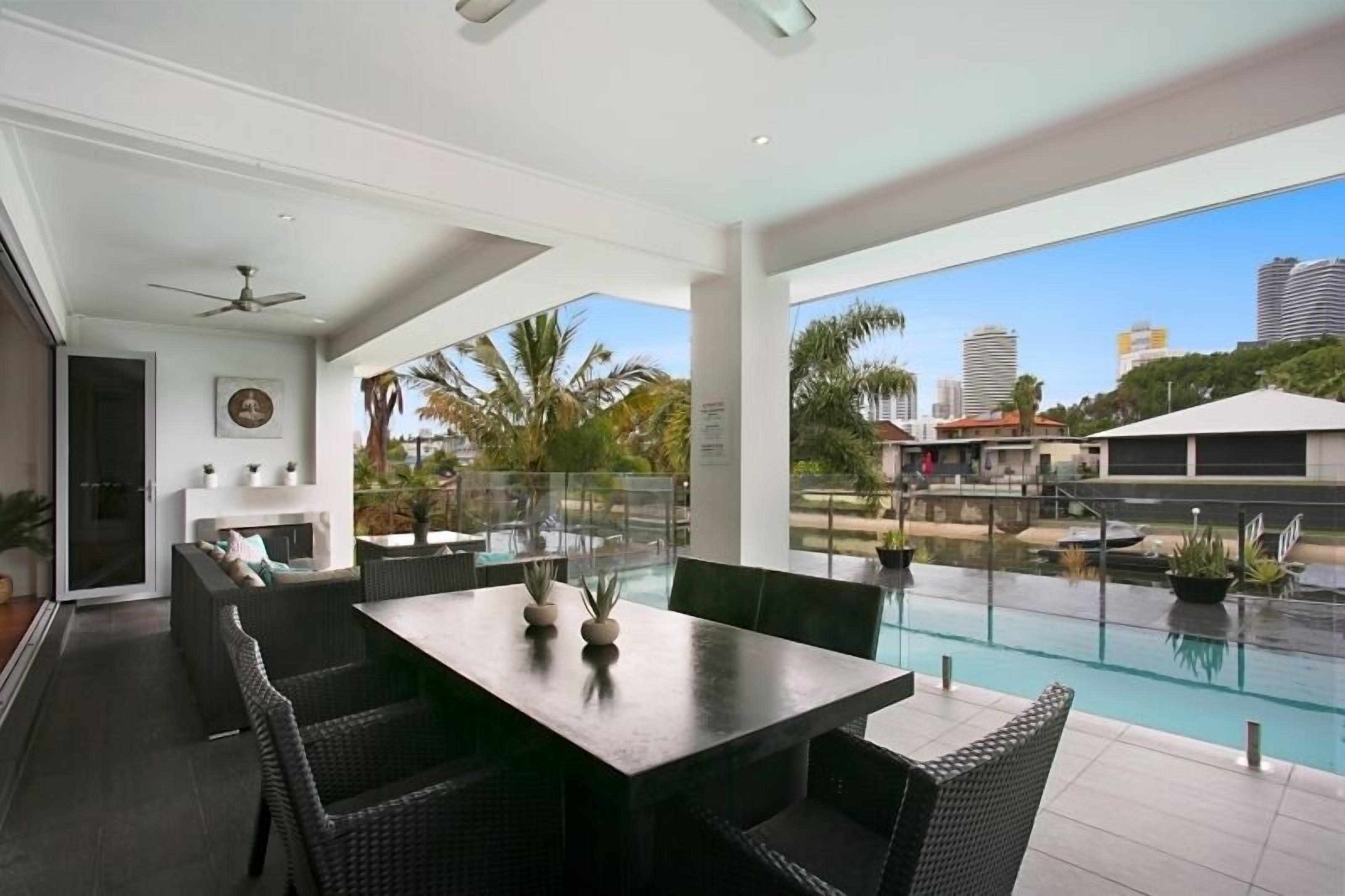 A modern outdoor dining area with a pool, wicker furniture, and a city view.