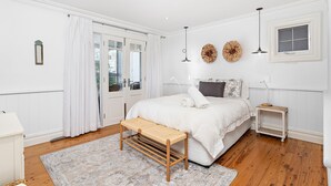 A bedroom with a bed, bedside table, bench, and a small table with a lamp. - Hamptons Escape - Magnificent views (Gerroa)