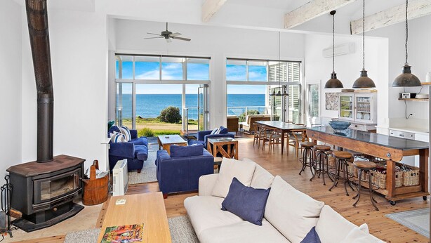 A spacious living area with a large window overlooking the sea, a cozy seating area with a fireplace, and a kitchen with a bar. - Hamptons Escape - Magnificent views (Gerroa)