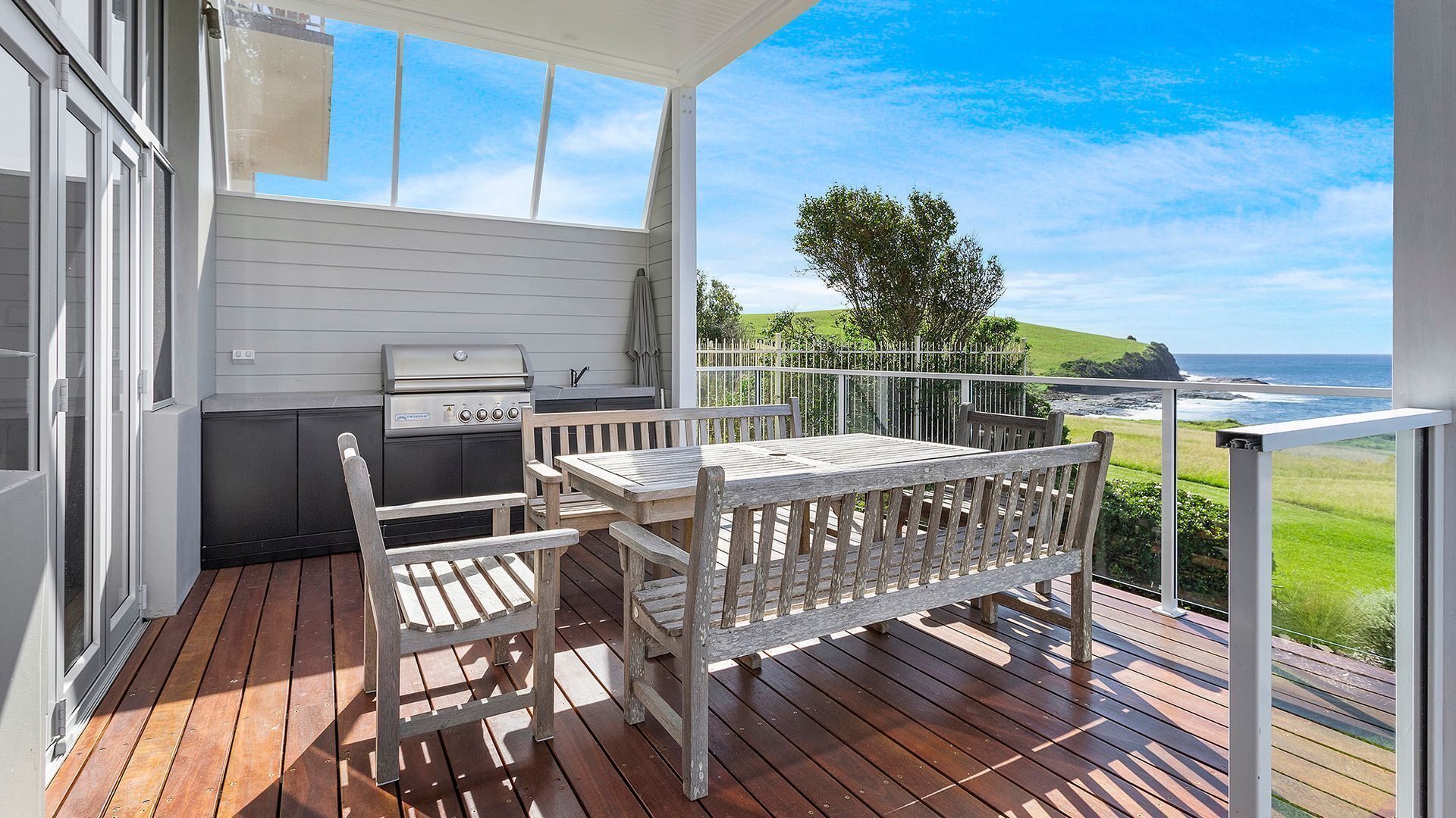 A balcony with a wooden table and chairs, a grill, and a view of the ocean.
