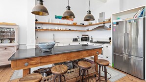 A modern kitchen with a central island, bar stools, a stainless steel refrigerator, and hanging pendant lights. - Hamptons Escape - Magnificent views (Gerroa)