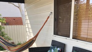 Een rieten bank met twee kussens, een hangmat en een houten terras.
