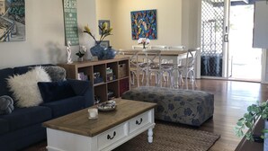 Een woonkamer met een blauwe bank, een houten salontafel en een eethoek met witte stoelen.