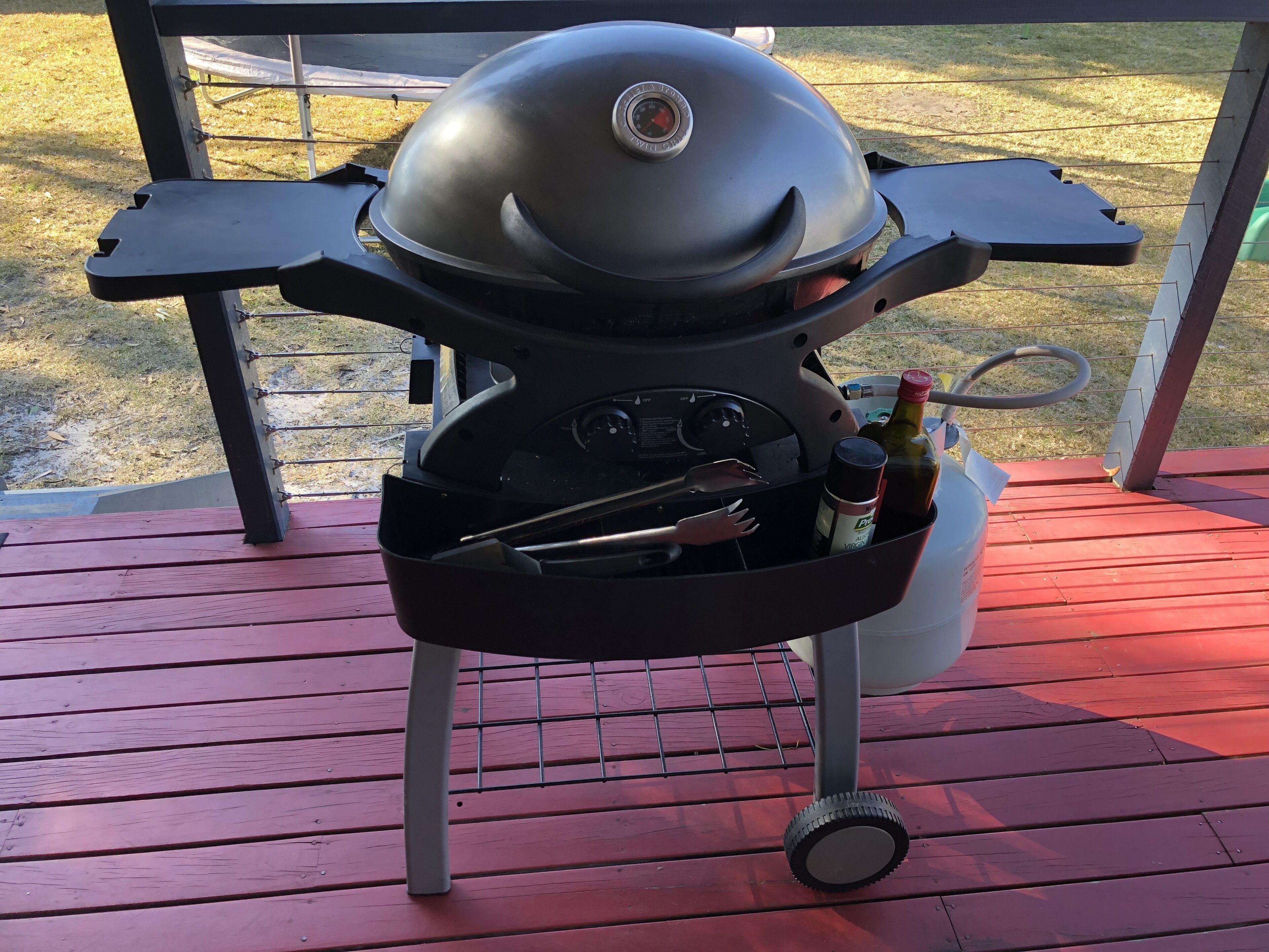 A barbecue grill with a built-in cooler, a bottle of wine, and a bottle of sauce.