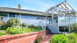 A modern building with a glass conservatory, a brick retaining wall, and a variety of plants. - Magnificent Views Over the Bay (Encounter Bay)
