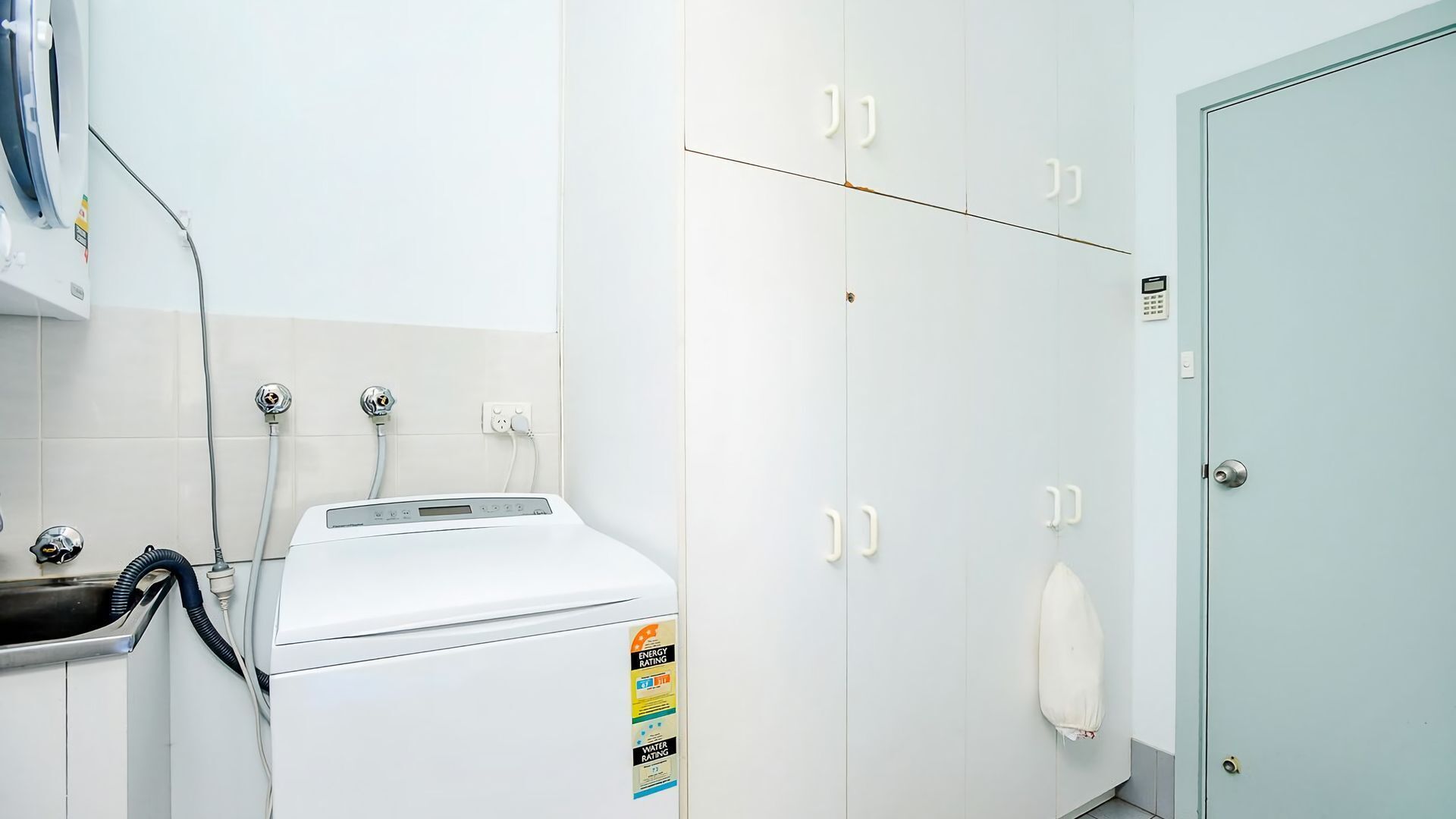 Een wasserette met een wasmachine, een wasbak en een deur waar een handdoek aan hangt.