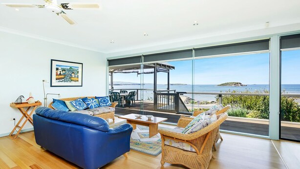 A spacious living room with a blue sofa, wicker chairs, and a view of the sea. - Magnificent Views Over the Bay (Encounter Bay)