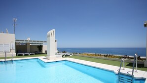 Ein Schwimmbecken mit klarem, blauem Wasser, Blick auf den Ozean und ein weißes Gebäude mit modernem Design.