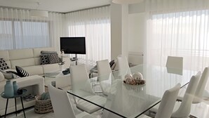 Ein modernes Wohnzimmer mit einem Glastisch, weißen Sofas und einem Flachbildfernseher.