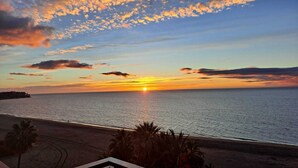 Ein Sonnenuntergangsblick von einem Balkon mit Blick auf einen Strand, Palmen und einen klaren Himmel.