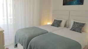 Ein Hotelzimmer mit zwei Betten, weißer Bettwäsche und einem Gemälde einer Straßenszene an der Wand.