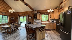 A log cabin-style kitchen with wooden cabinets, a central island, and a dining area with chairs. - Montana Escape Cabin in the woods (Bigfork)