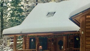 A log cabin with a snow-covered roof and a porch with a chair. - Montana Escape Cabin in the woods (Bigfork)