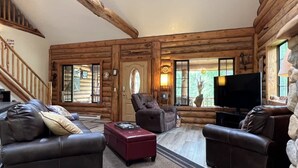 A log cabin interior with a fireplace, leather sofas, a flat-screen TV, and a staircase. - Montana Escape Cabin in the woods (Bigfork)