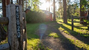 A wooden post with a house number sign, a gravel path, and a wooden fence in a forested area.