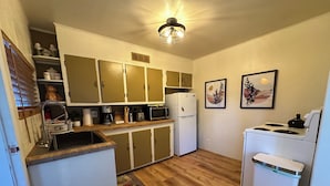 A compact kitchen with a refrigerator, microwave, stove, and sink. There are cabinets, a ceiling light, and a rug on the floor.
