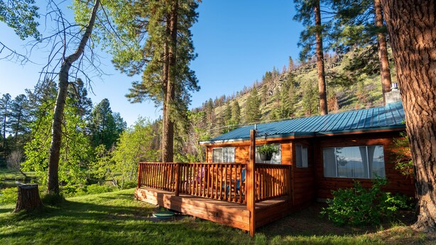 A cabin with a wooden deck, surrounded by trees and a clear sky.
