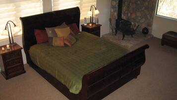 A bedroom with a large bed, a stone fireplace, and a window with blinds.