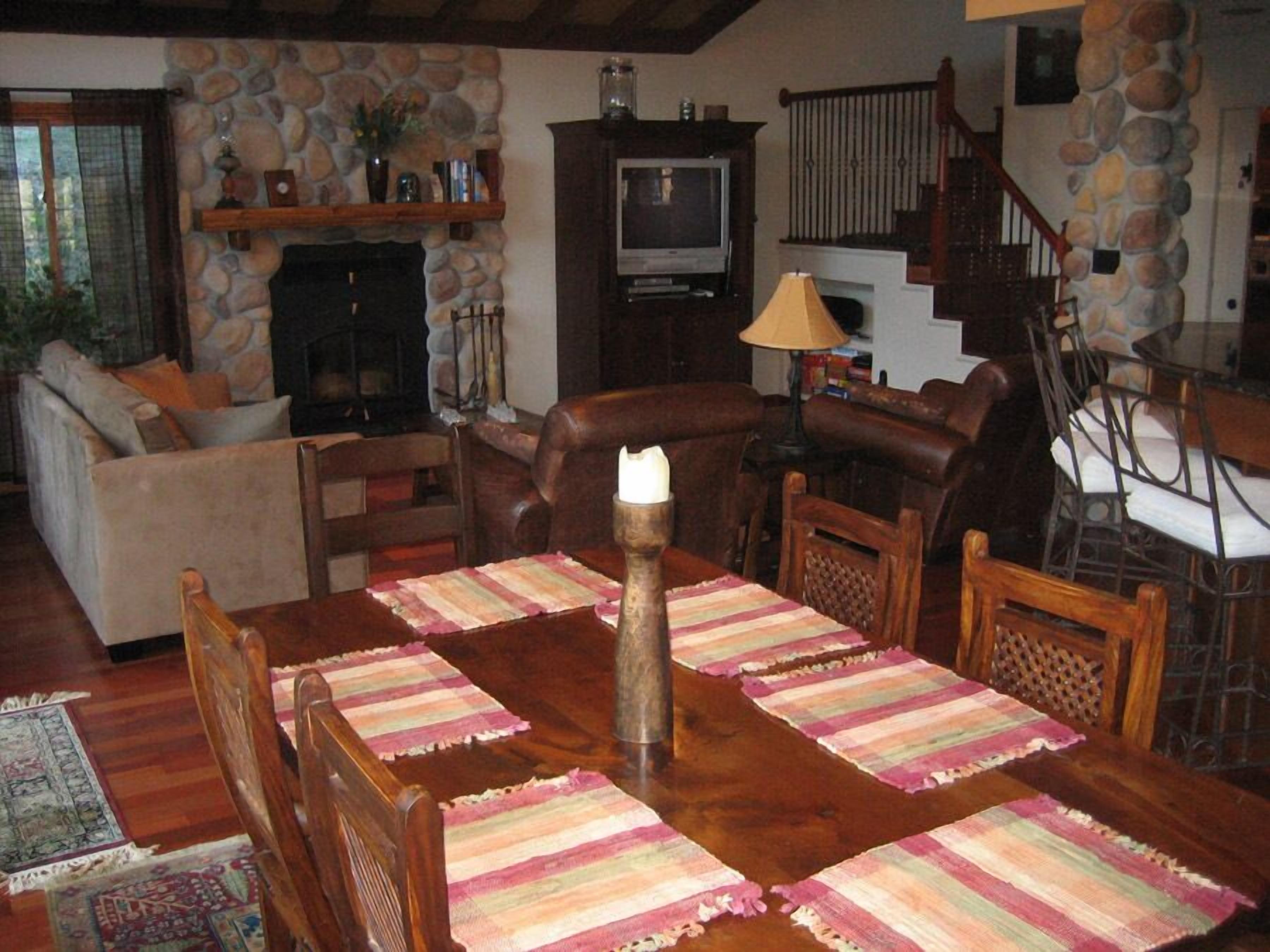 A cozy living room with a stone fireplace, a television, and a dining area with a wooden table and chairs.