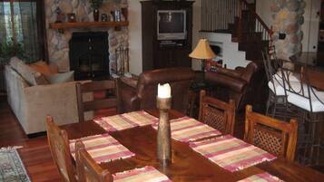 A cozy living room with a stone fireplace, a television, and a dining area with a wooden table and chairs.