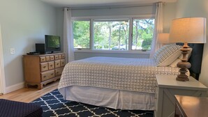 Une chambre à coucher avec un lit, une commode, une télévision et une fenêtre avec des rideaux.