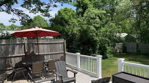Une terrasse en bois avec des meubles d’extérieur, un parasol rouge et une rambarde blanche.