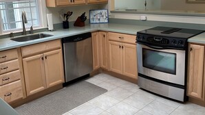 Une cuisine moderne avec des meubles en bois, un lave-vaisselle en acier inoxydable, un four et des luminaires suspendus.