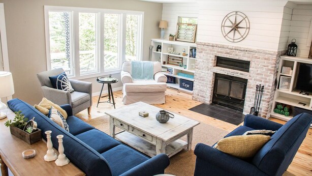 A living room with a fireplace, blue sofas, a coffee table, and a bookshelf. - Amazing Views All Seasons White Lake/Channel Spacious Easy Walk to Lake Michigan (Montague)
