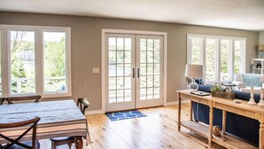 A spacious room with a dining table, chairs, a sofa, and a coffee table. There are large windows and a door with glass panels. - Amazing Views All Seasons White Lake/Channel Spacious Easy Walk to Lake Michigan (Montague)