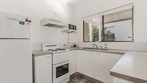 A compact kitchen with white cabinetry, a built-in microwave, a stove, and an oven.
