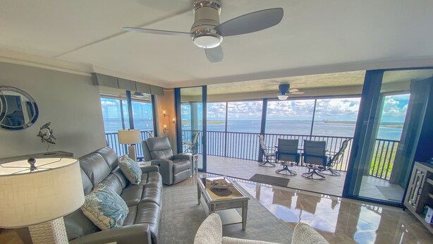 A spacious living area with a leather sofa, armchairs, and a coffee table. A large window offers a view of the ocean. - Sanibel Harbour 817: Wrap-around lanai-Amazing Water Views! Enjoy private beach &activities nearby. (Fort Myers)