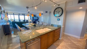 A spacious kitchen with a granite countertop, wooden cabinets, and a built-in dishwasher. - Sanibel Harbour 817: Wrap-around lanai-Amazing Water Views! Enjoy private beach &activities nearby. (Fort Myers)