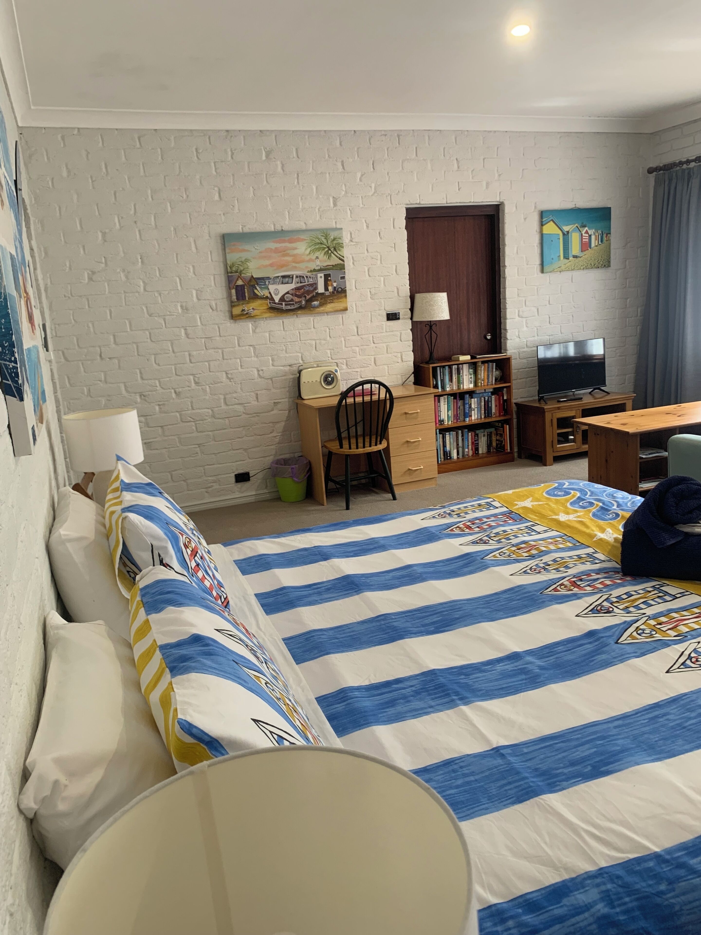 Une chambre à coucher comprenant un lit, un bureau, une chaise, une bibliothèque, un téléviseur et une porte.