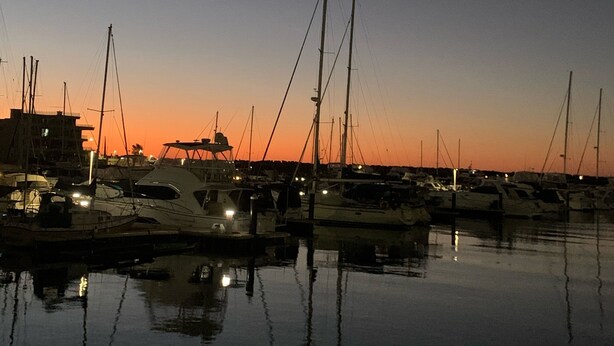 Un puerto deportivo al atardecer, con barcos amarrados y una luna creciente en el cielo.