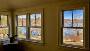 Ein Zimmer mit drei Fenstern, jedes mit Blick auf eine Landschaft aus Bäumen und einem Gewässer.
