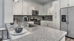 A modern kitchen with white cabinets, a granite countertop, stainless steel appliances, and pendant lighting. - Centrally located in Uptown Charlotte.  Gym, Pool and Free Parking.  Walk everywhere! (Charlotte)