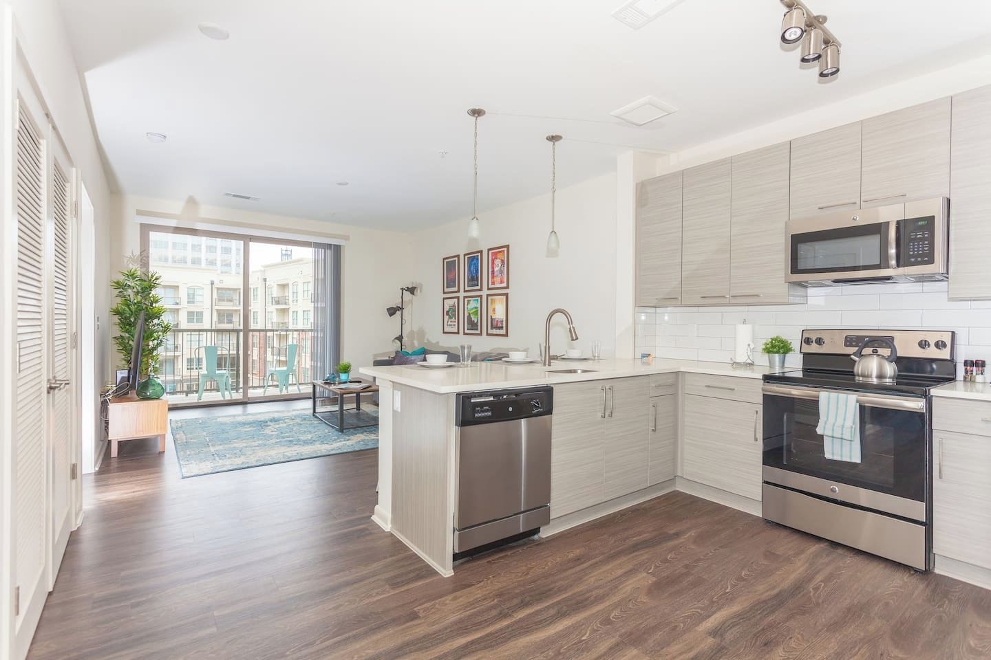 A modern kitchen with a dishwasher, stove, microwave, and a large window overlooking a balcony.