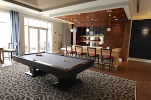 A pool table in a room with a patterned carpet, a bar area with stools, and a kitchen in the background. - Uptown Charlotte Pool View - 24/7 Fitness Center (Charlotte)